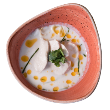 Overhead of a red bowl with Tom Kha Coconut Soup prepared with galangal, lemon grass, kaffir, lime leaves, coconut meat and Thai spices in a broth of rich coconut milk.